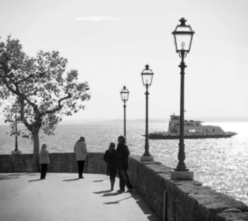 Lago di Garda in bianco e nero: tensione tra balustrata e silhouettes sul mare luminoso del tramonto