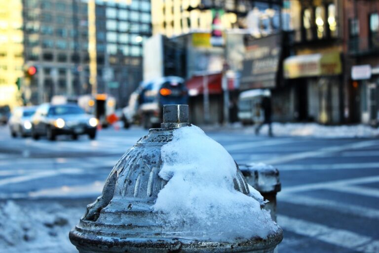 Idrante urbano in primo piano: neve, texture e ritmo fra strade frenetiche
