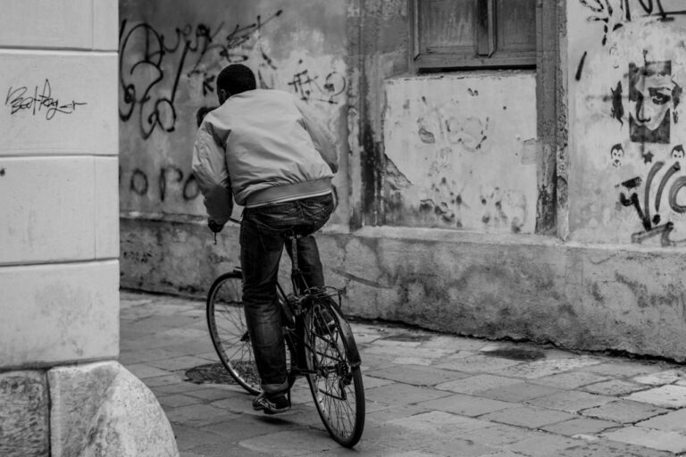 Urgenza in bianco e nero: ciclista tra muri graffiati e marciapiede deteriorato