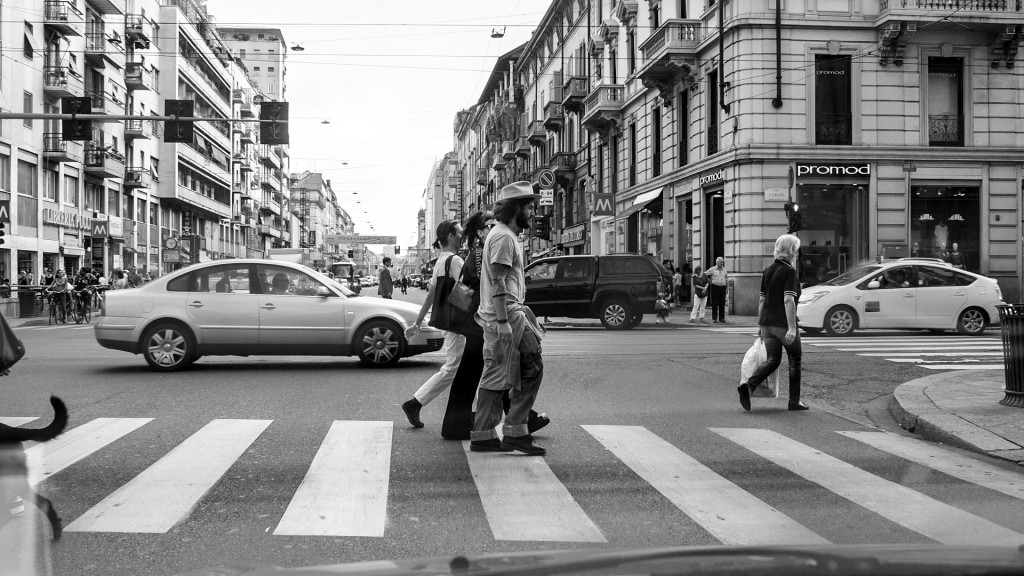 Scena di attraversamento: umanità in bianco e nero tra strisce e facciate
