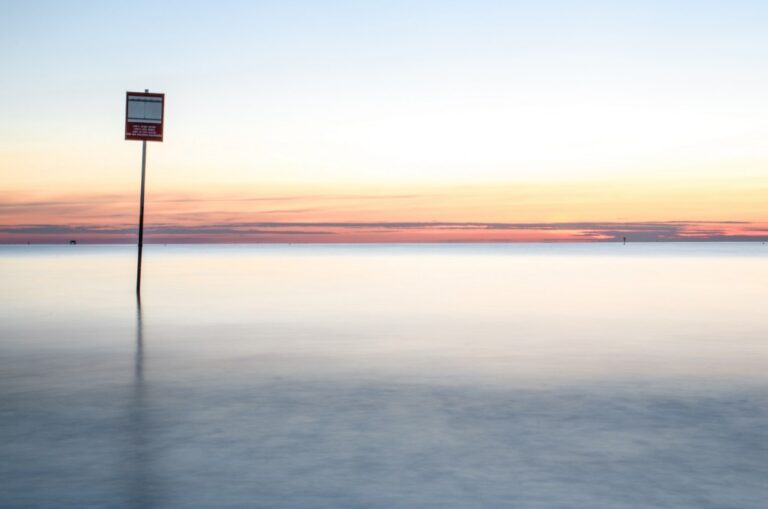 Minimalismo dorato: palo, riflessione e mare in luce cremosamente stoppata