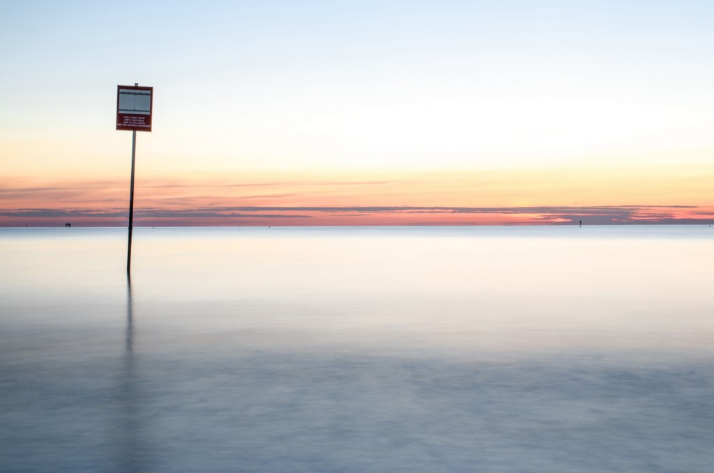 Minimalismo dorato: palo, riflessione e mare in luce cremosamente stoppata