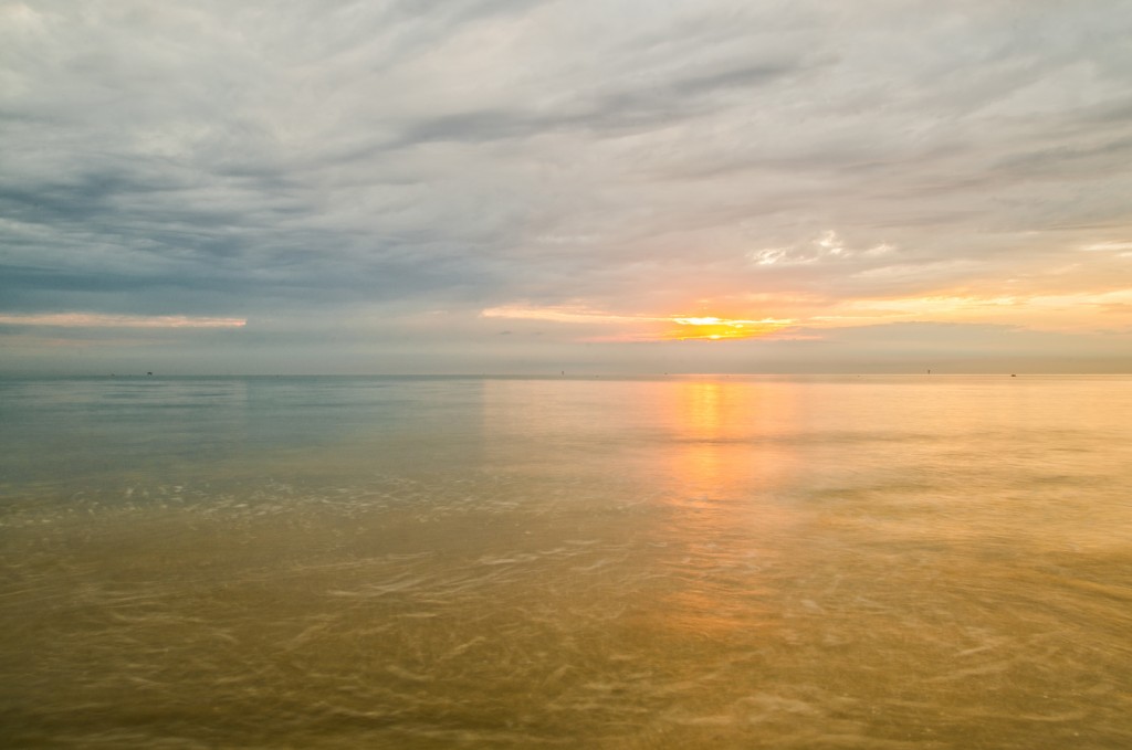 Transizione di luce tra mare ambrato e cielo plumbeo: quiete e riflessi baluginanti