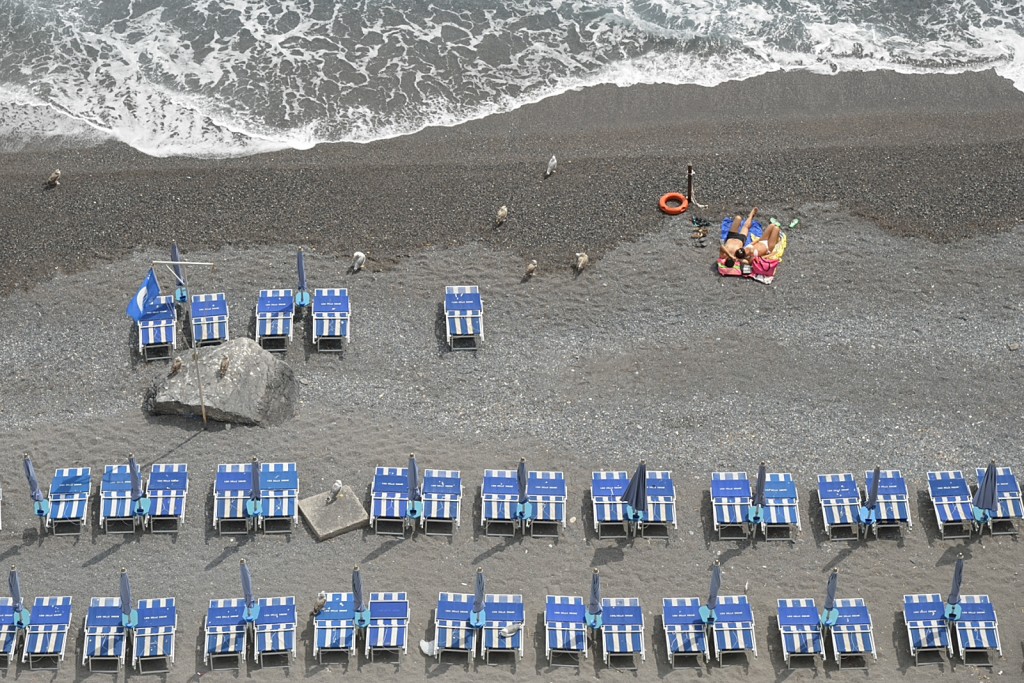 Geometria ordinata e figure distanti: sabbia, lettini blu e mare in sospensione