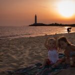 Sguardi in buttero tramonto: gioco tra sorelline, mare e faro