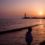 Tramonto al faro: siluette, riflessi e quiete marina a foto finita in luce crepuscolare