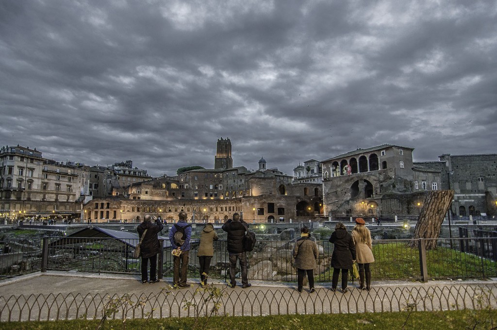 Roma tra dimensioni: figure moderne e ruderi narranti sotto cielo carico di nuvole