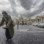 Solitudine urbana: una signora tra pioggia, pietra e movimento in bianco e nero