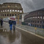 Pioggia su Roma: due passanti tra bara di cantieri e Colosseo in controluce
