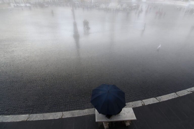 Inverno romano: ombrello blu, riflessi e vuoto urbano in pioggia filtrata