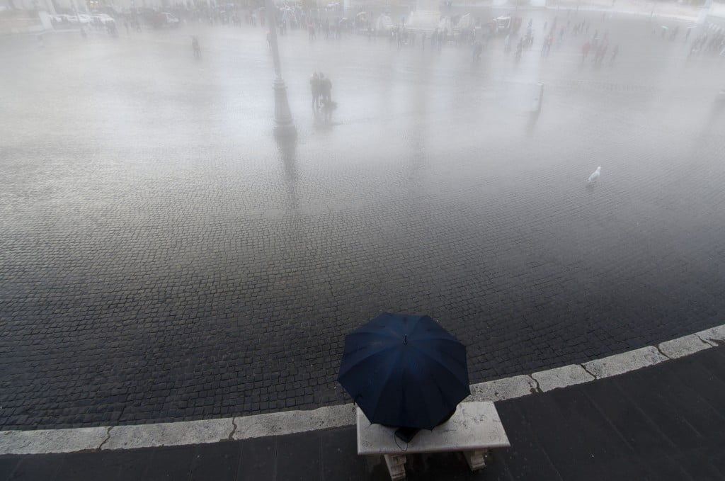 Inverno romano: ombrello blu, riflessi e vuoto urbano in pioggia filtrata