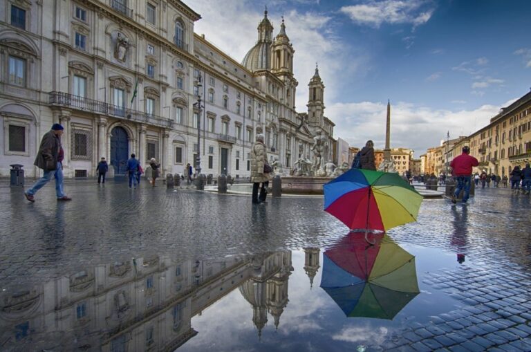 Roma sotto pioggia: riflessi, ombrelli e silenzio urbano in una via pavimentata di luce e colore